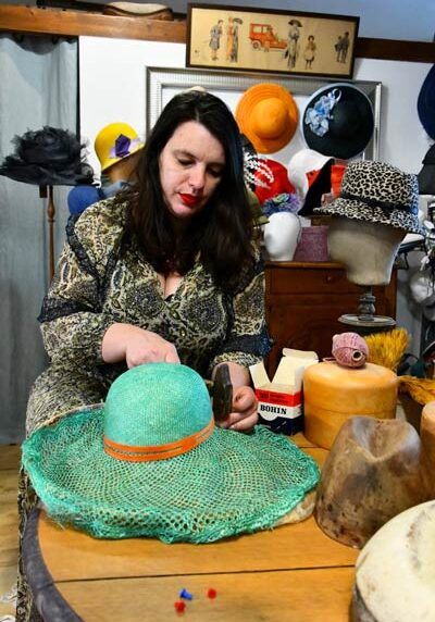 Portrait d'Efti Cianko, créatrice de mode et chapelière à Blois, dans son atelier entourée de ses créations.